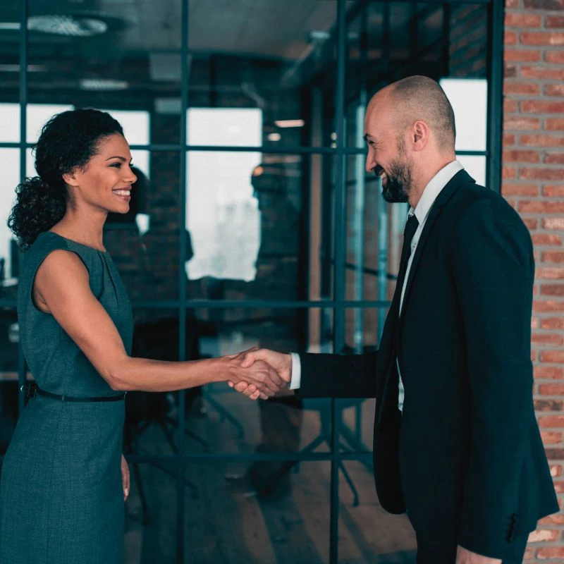 Two business professionals shaking hands in a modern office setting